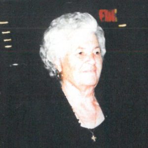 An older woman in a black dress standing in front of a crowd.