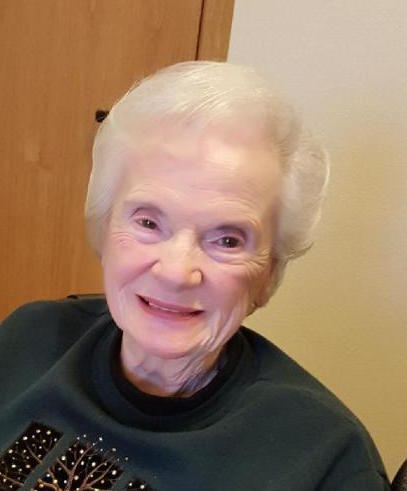 An older woman smiles while sitting in a chair.