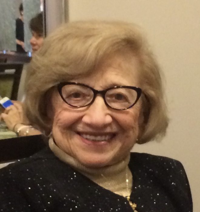 An older woman wearing glasses and sitting at a table.