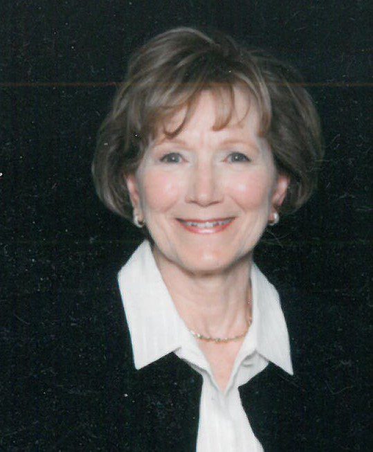 A woman in a black suit and white shirt is smiling.