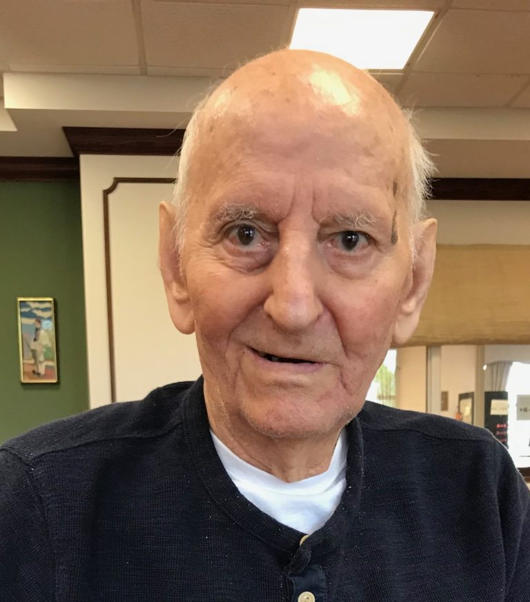 An older man in a blue shirt sitting at a table.