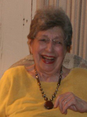 An older woman wearing a yellow shirt and a necklace.