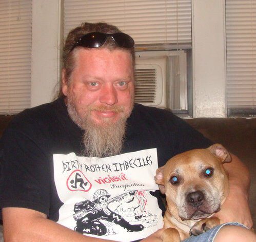 A man with a beard sitting on a couch with a dog.