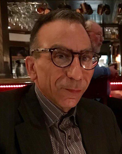 A man in glasses sitting at a bar.