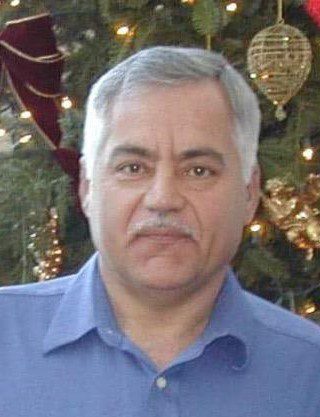 A man in a blue shirt standing in front of a christmas tree.