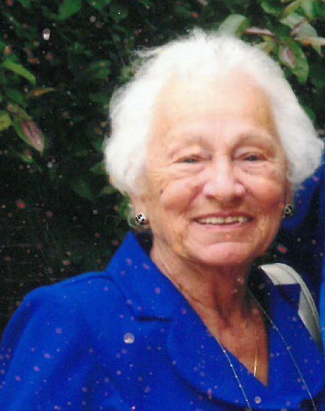 An older woman in a blue jacket is smiling for the camera.