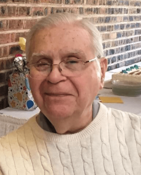 An older man in a white sweater sitting at a table.