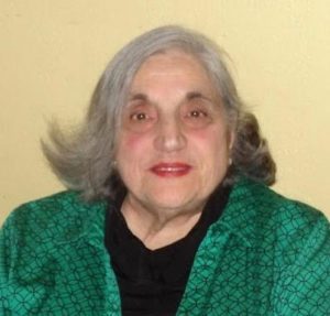 An older woman wearing a green shirt and black jacket.