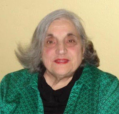 An older woman wearing a green shirt and black jacket.