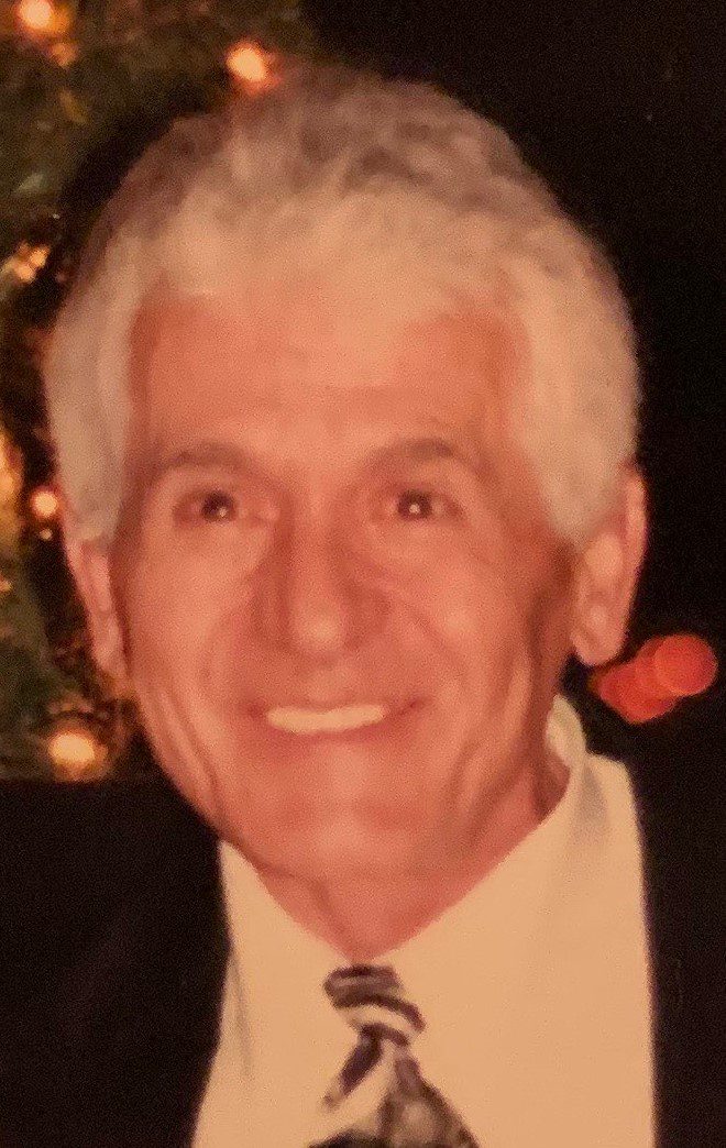 An older man smiling in front of a christmas tree.