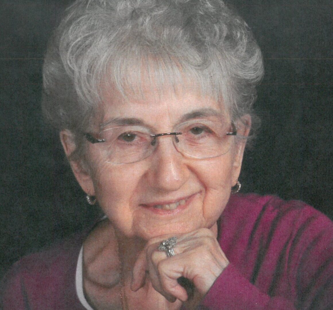 An older woman in glasses is posing for a photo.