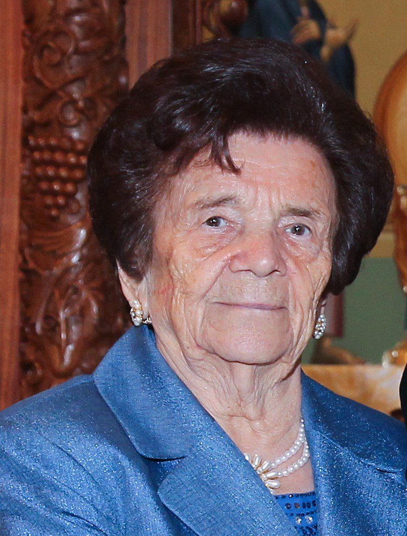 An older woman wearing a blue suit and a pearl necklace.