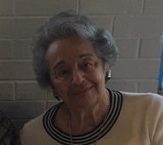 Two older women sitting next to each other in front of a brick wall.