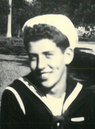 A young man in a sailor's uniform smiling.