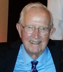 An older man in a suit and tie smiles for the camera.