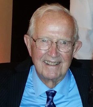 An older man in a suit and tie smiles for the camera.