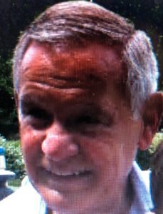 A man in a white shirt is smiling at the camera.