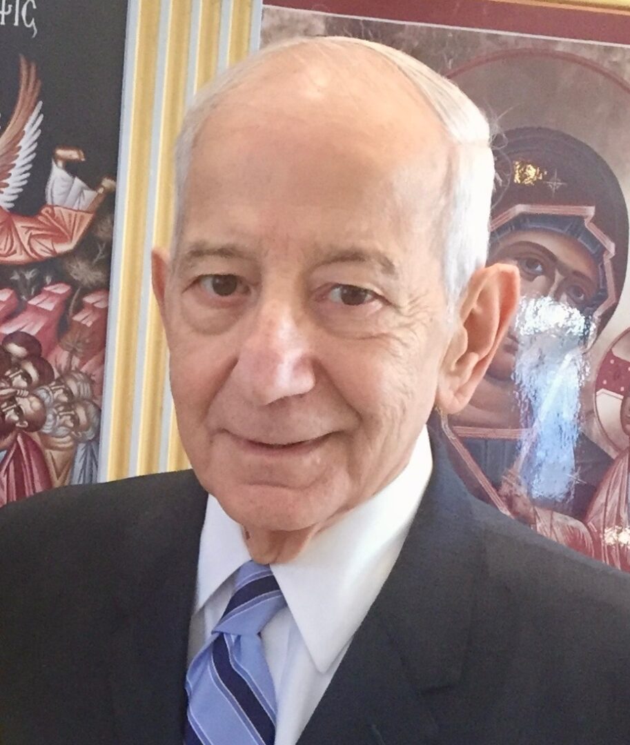 An older man in a suit and tie standing in front of a painting.