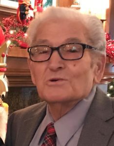 An older man wearing glasses and a tie in front of a christmas tree.
