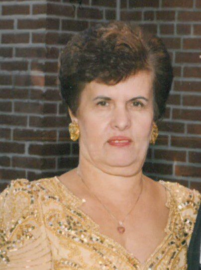A woman in a gold dress standing next to a brick wall.