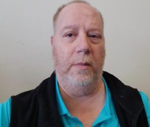 A man with a beard is standing in front of a wall.
