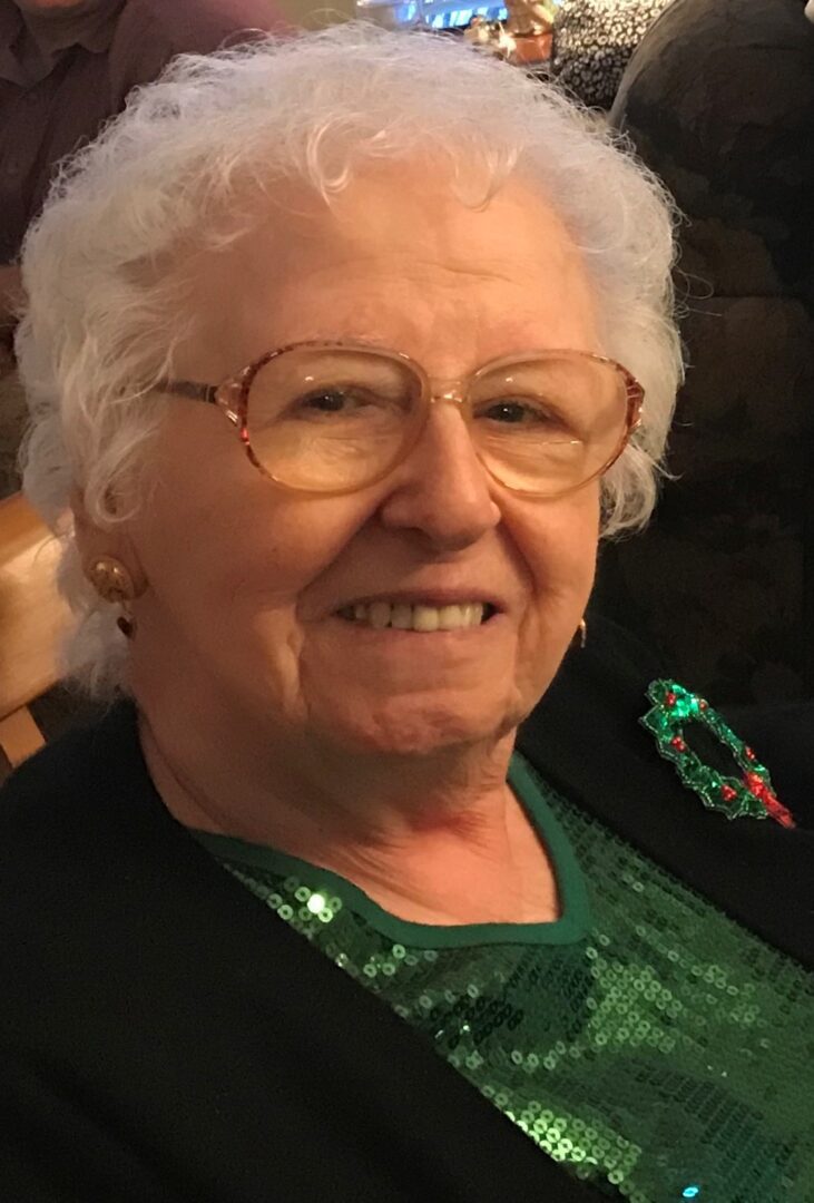 An older woman wearing glasses and a green top.