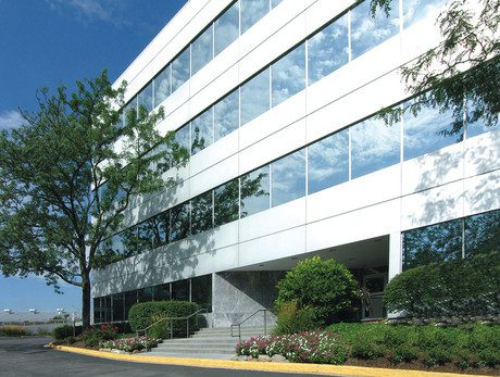A white office building with trees and shrubs.