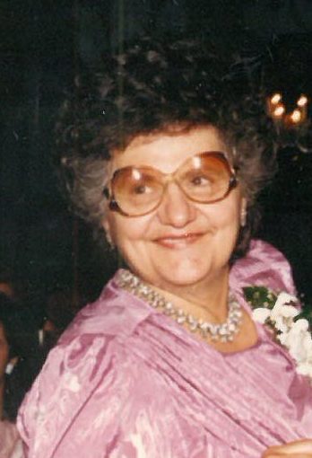 An older woman wearing glasses and a purple dress.