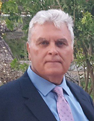 A man in a suit and tie standing in front of a tree.
