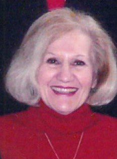 An older woman in a red turtleneck shirt smiling.