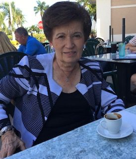 An older woman sitting at a table with a cup of coffee.