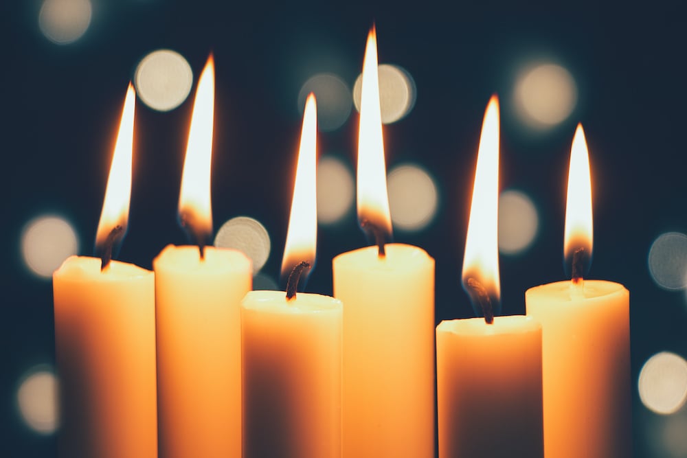 Five candles lit in front of a bokeh background.