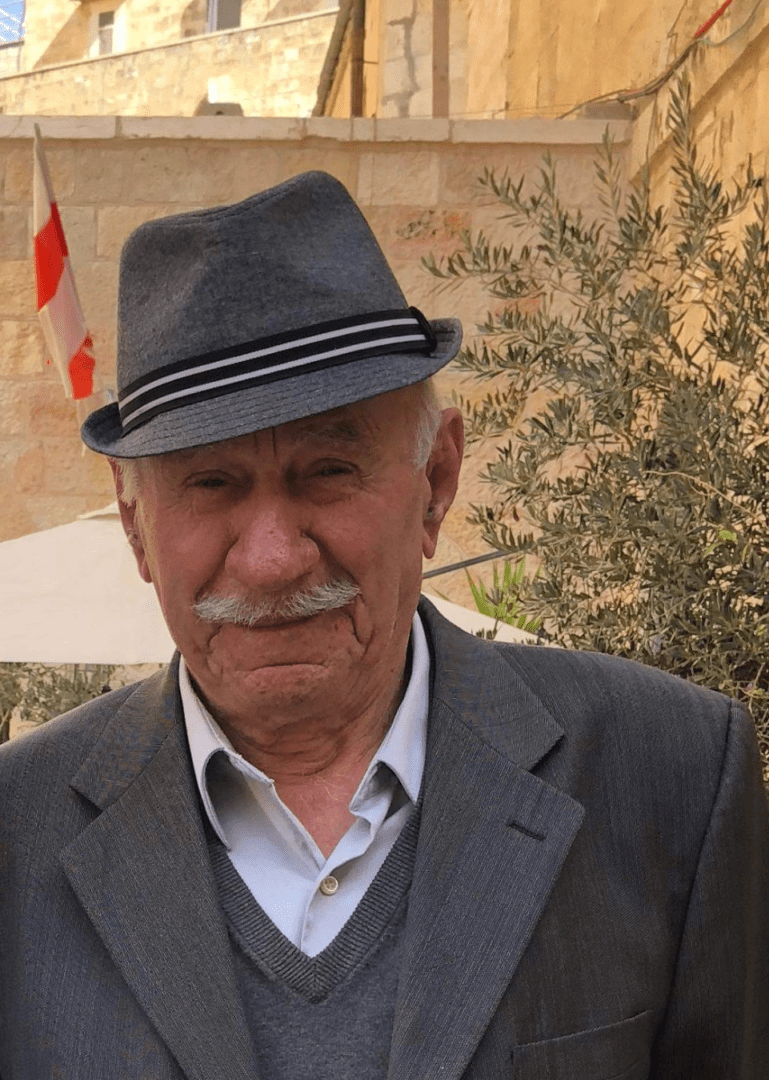 An older man in a hat standing in front of a building.