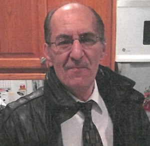 A man in a black jacket standing in a kitchen.