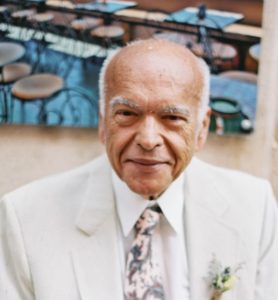 An older man in a white suit and tie.