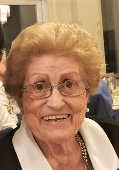 An older woman smiles for the camera while sitting at a table.