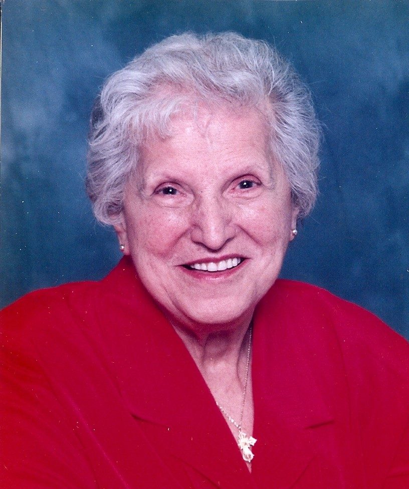 An older woman in a red shirt smiles for the camera.