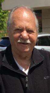 An older man with a mustache in front of a building.