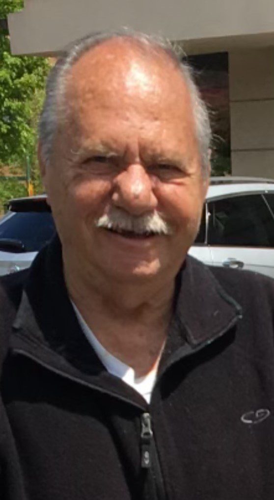An older man with a mustache in front of a building.