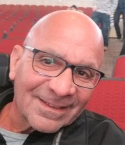 A bald man with glasses smiling in an auditorium.