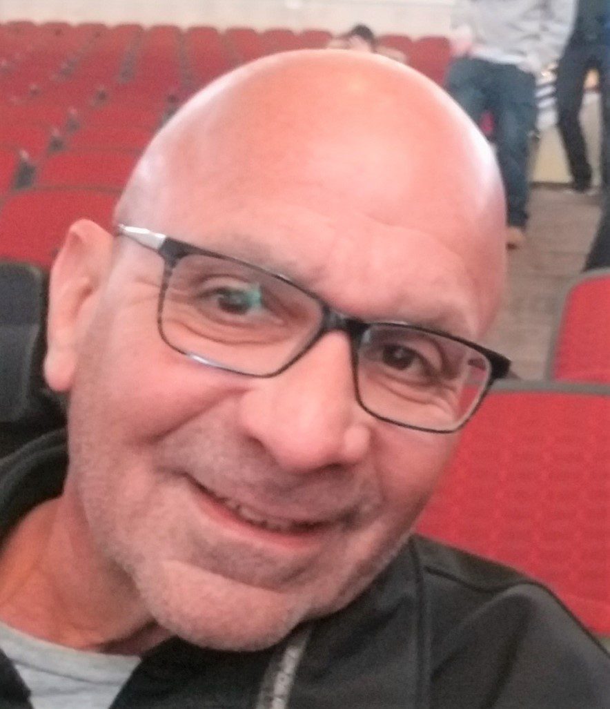 A bald man with glasses smiling in an auditorium.
