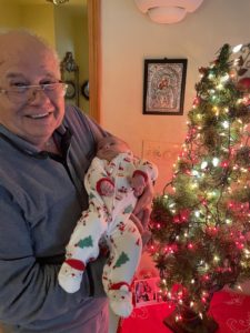 An older man holding a baby in front of a christmas tree.