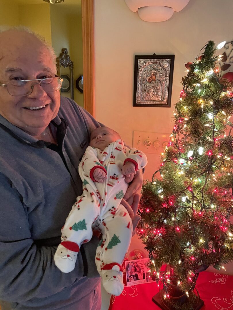 An older man holding a baby in front of a christmas tree.