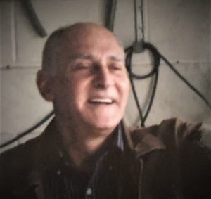 A man in a brown jacket is smiling in a garage.