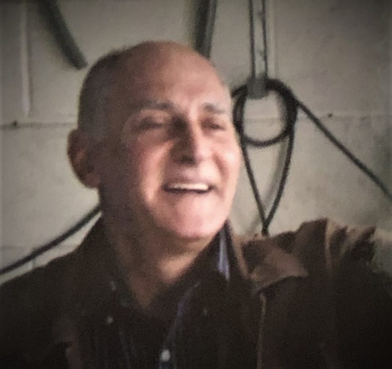 A man in a brown jacket is smiling in a garage.