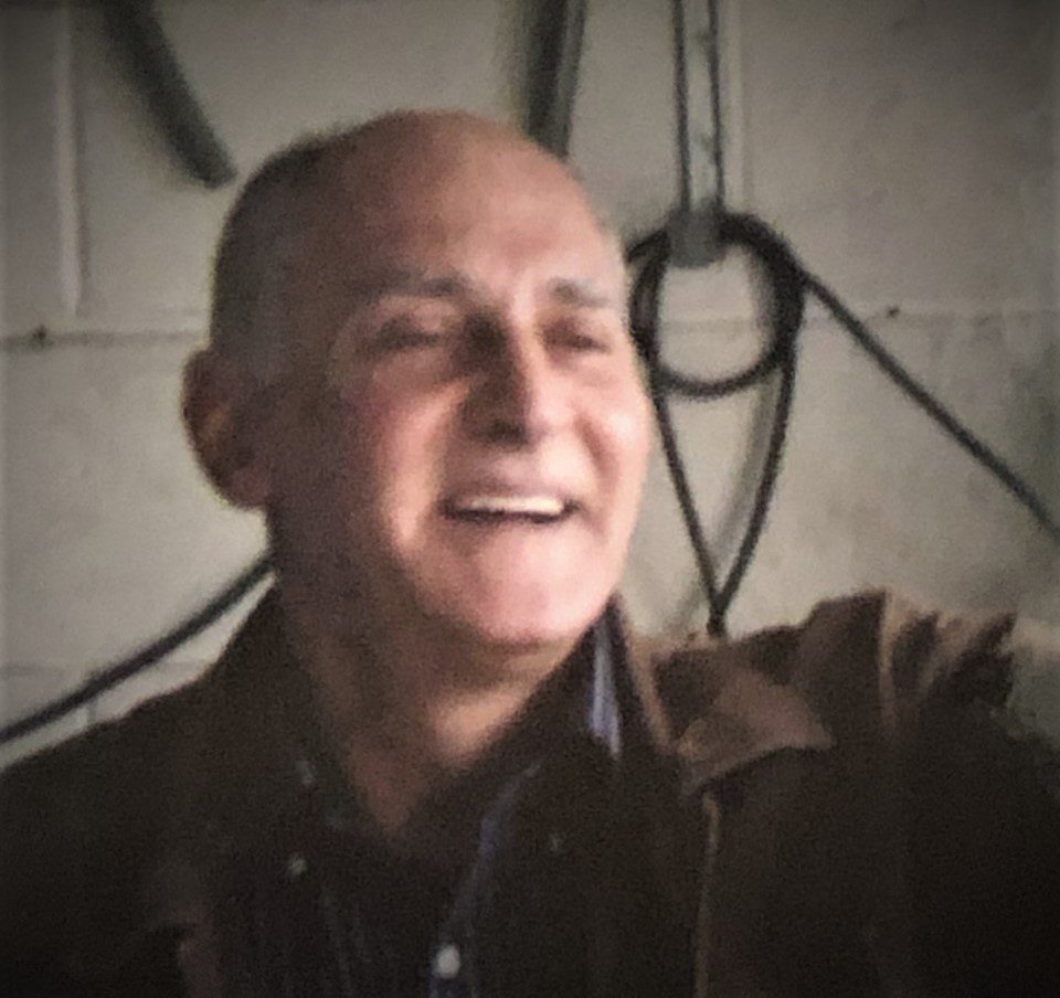 A man in a brown jacket is smiling in a garage.