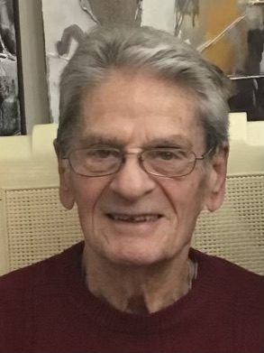 An older man in a red sweater smiles for the camera.