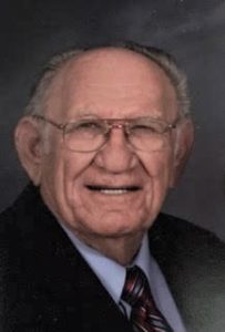 An older man in a suit and tie is smiling.