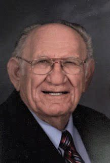 An older man in a suit and tie is smiling.