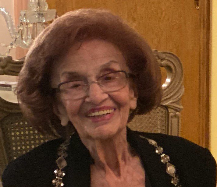 An older woman with glasses sitting in a chair.